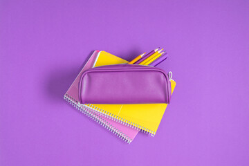 Purple pencil case with pencils and notebooks on purple background. Back to school. Flat lay, top view, copy space - obrazy, fototapety, plakaty