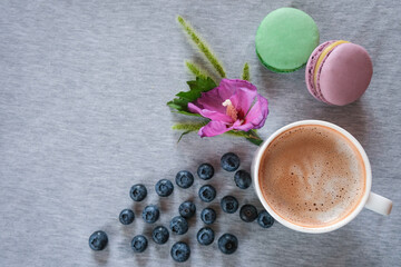 Obraz na płótnie Canvas Cozy home composition. Cup of coffee or cocoa hot drink and macaroons, flowers, blueberries on a gray table. Top view, copy space 