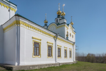 Fototapeta na wymiar Rural restored old church against the blue sky on a spring sunny day. Historic church with golden domes in the village of Klyuchi (Perm Territory, Russia). Reflection of the sun in gold domes