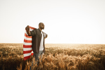 African american young man holding USA national flag through wheat field