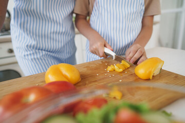 Close up of a woman and girl cutting vegetables for salad in kitchen