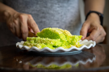 Pandan green cake with butter crumbs in a white plate with a person behind.