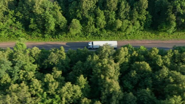 The top view of the white lorry. The interregional highway is surrounded by dense deciduous forests. The concept of multimodal transportation, groupage cargoes. High quality. 4k footage.