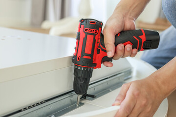 man assembling white table furniture at home using cordless screwdriver