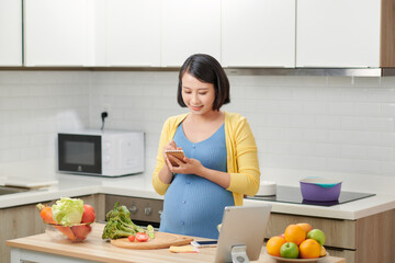 pregnant woman using a tablet computer in her kitchen