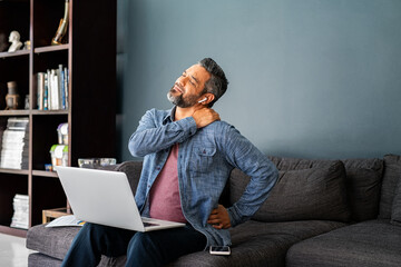 Exhausted ethnic man stretching neck and back after many hours spent working