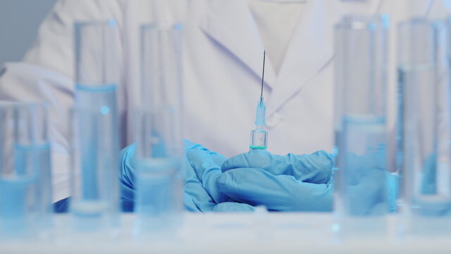 Close-up of a doctor's hand in medical gloves holding a syringe with a vaccine, test tubes in the foreground