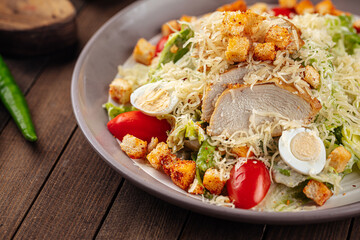 Plate of caesar salad with chicken and lettuce on wooden background