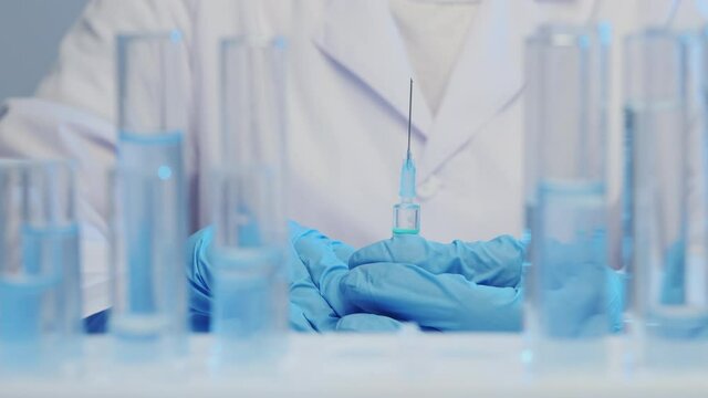 Close-up of a doctor's hand in medical gloves holding a syringe with a vaccine, test tubes in the foreground