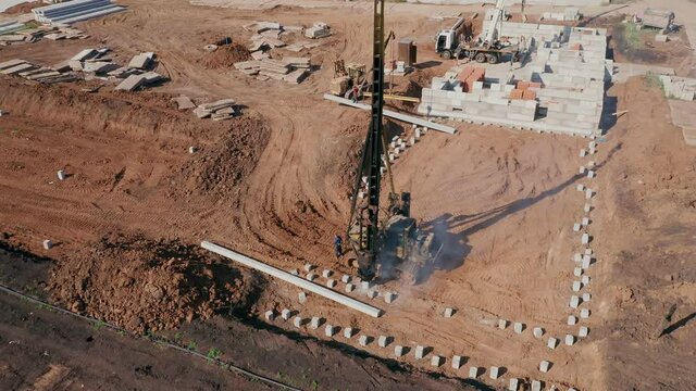 Pile driving machine installs piles in the ground. Activities of the contractor's company on the construction site. Unfinished foundation of the house in the background. High quality. 4k footage.