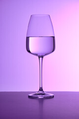 A close-up of a glass filled with pure water against the purple background. Plain surface, no splashes, colored light. Restaurant glassware, serve, romance, passion, love, party, beverage.