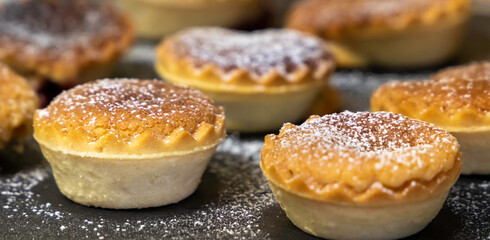 small tartlets pastries with almond frangipane and powdered sugar scattered over black stone surface - selective focus - close up