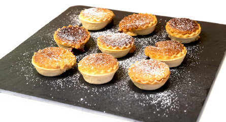 small tartlets pastries with almond frangipane and powdered sugar scattered over black stone surface - selective focus