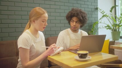 Restaurant employees working on laptop and writing notes, receiving online order