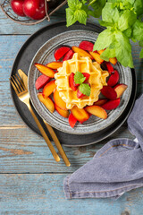 Traditional classic Belgian or Brussels waffles with red plums in a ceramic plate on a blue wooden culinary background top view	