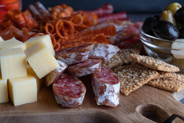 Cutting board with ham, salami, cheese, crackers and olives on a dark stone background. Close-up view of the delicious Italian dry sausage.