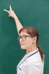 school teacher young pretty woman in a white blouse and glasses with chalk in her hand in the classroom on the background of a green blackboard. portrait