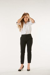 A girl in a white shirt stands on a white isolated background and holds her head.