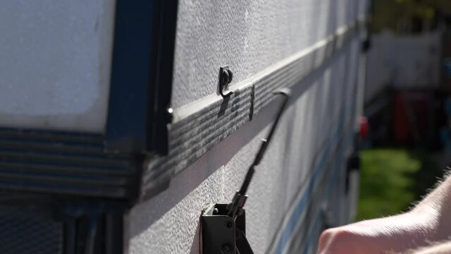 A hand removes a clasp on a tent trailer getting ready to set it up and go camping 