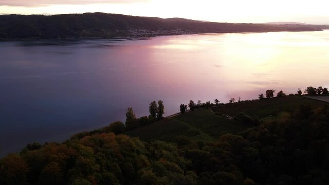 Apple plantation and forests on a wide river, the colourful sunrise is reflected in the water - drone flight 