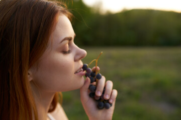 cheerful pretty woman outdoors eating grapes fresh air
