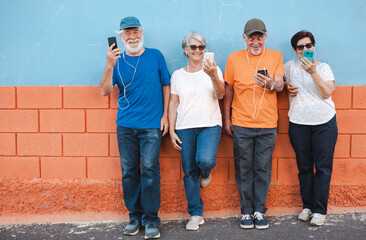 Group of smiling mature people standing outdoor using mobile phone with earphones. Four elderly...