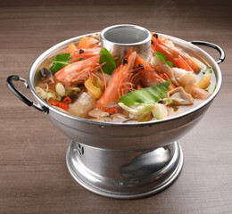 thai clear tom yum spicy chilli hot soup with seafood, meat and vegetables in hot pot in wood background asian halal menu