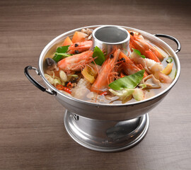 thai clear tom yum spicy chilli hot soup with seafood, meat and vegetables in hot pot in wood background asian halal menu
