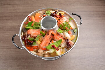 thai clear tom yum spicy chilli hot soup with seafood, meat and vegetables in hot pot in wood background asian halal menu