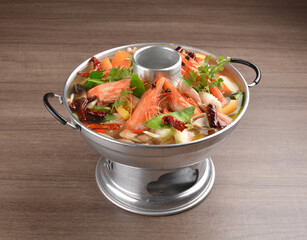 thai clear tom yum spicy chilli hot soup with seafood, meat and vegetables in hot pot in wood background asian halal menu