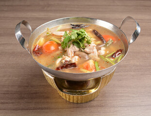 thai clear tom yum spicy chilli hot soup with seafood, meat and vegetables in hot pot in wood background asian halal menu