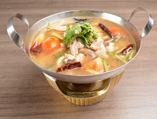 thai clear tom yum spicy chilli hot soup with seafood, meat and vegetables in hot pot in wood background asian halal menu