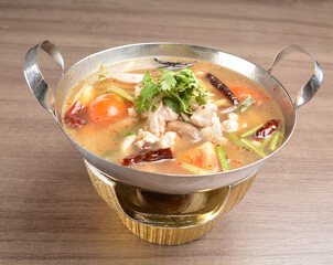 thai clear tom yum spicy chilli hot soup with seafood, meat and vegetables in hot pot in wood background asian halal menu