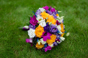 Wedding bright bouquet on the green grass. White, yellow, orange, blue and purple roses in a bouquet. Wedding attributes, symbol. Close-up. Advertising bouquet
