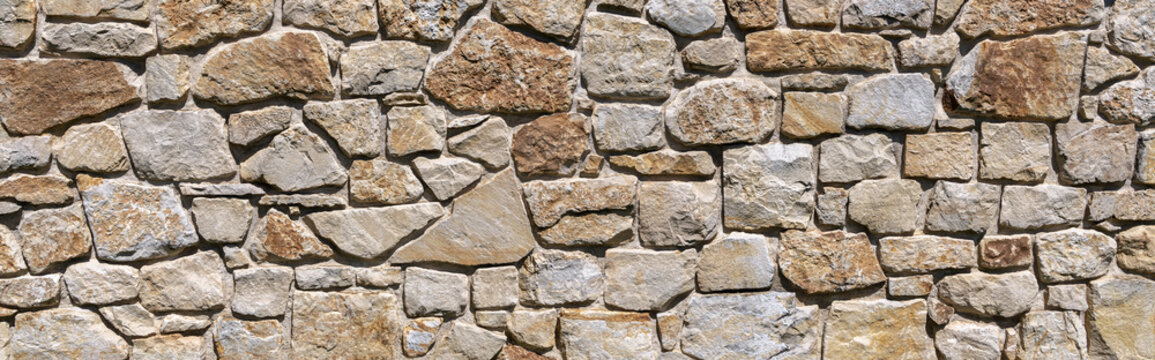 Braun graue Panorama Natursteinmauer mit tiefen Fugen im Sonnenschein