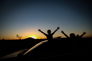 Silhouette landscape image of children on roof of SUV vehicle on country road with Pyramid Hill in...