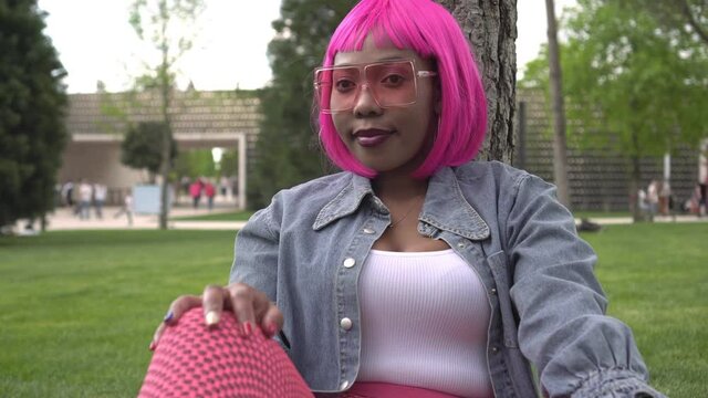 Young informal black woman wearing pink wig and glasses outdoors