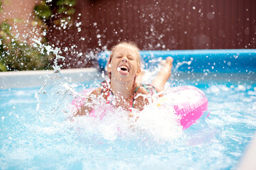 Fototapeta na wymiar Little girl squirts in an inflatable pool in the country