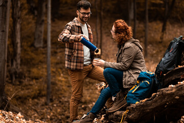 Young couple with backpack drinking tea after hiking in forest.