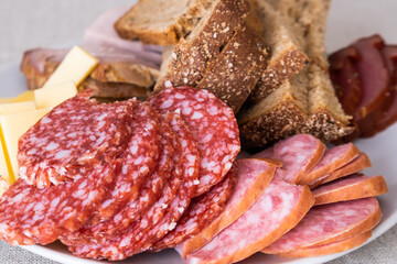 sliced smoked pork, bread, sausage, cheese on plate