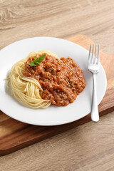 Close up a fork with spaghetti and red sauce in white dish on cutting board
