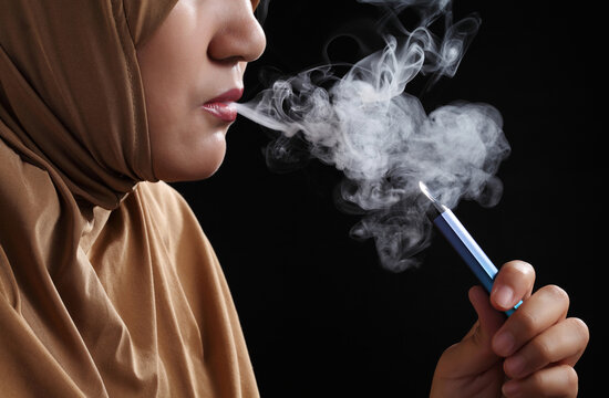 Close up young muslim woman smoking e-cigarette on black background