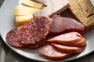 sliced smoked pork, bread, sausage, cheese on plate