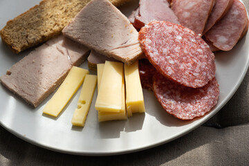 sliced smoked pork, bread, sausage, cheese on plate