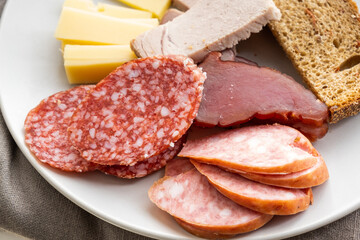 sliced smoked pork, bread, sausage, cheese on plate