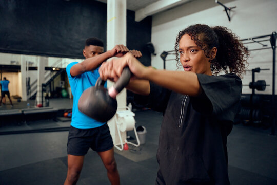 African American male personal trainer instructing African American female with a kettlebell routine in the gym. Mixed race friends doing cross training together. High quality photo