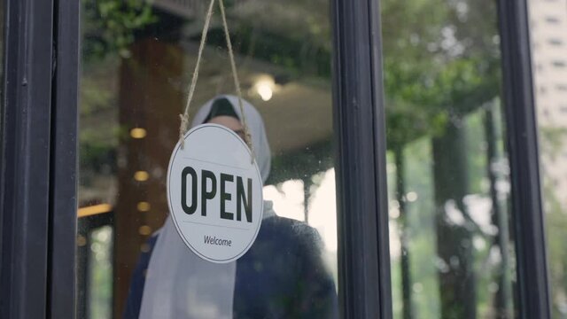 Young Asian Muslim Woman Wearing Hijab, Turning Sign To Closed The Coffee Shop Or Restaurant Due To Coronavirus Crisis. Female Muslim Business Owner Changing Sign From Open To Closed.