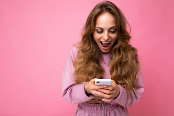 Photo shot of surprised amazed attractive positive good looking young woman wearing casual stylish outfit poising isolated on background with empty space holding in hand and using mobile phone