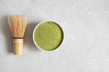 Matcha green tea on a gray background. Matcha tea powder and bamboo whisk. Traditional Japanese drink. Copy space, top view, flat lay.