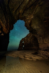 imagen nocturna con un arco de piedra de la playa de las catedrales con las estrellas de fondo y el mar en los pies